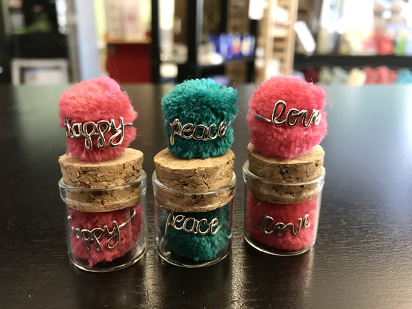 happy, peace, love wire rings with brightly colored pom-pom in glass and cork jar