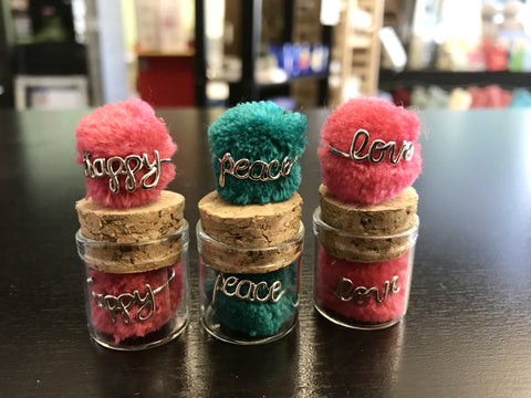 happy, peace, love wire rings with brightly colored pom-pom in glass and cork jar